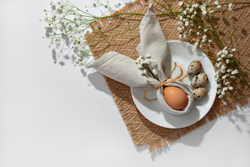 Minimalist Easter aesthetic table setting, egg decorated with bunny ears napkin on white plate. Neutral floral background with copy space. Holiday branding spring template or banner design