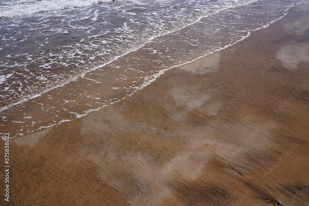 Wellen laufen über den Sand am Strand und die Wolken spiegeln sich im Sand