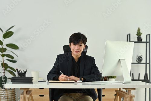 Portrait of young start up businessman in elegant suit sitting at his workplace in the modern office and smiling to camera