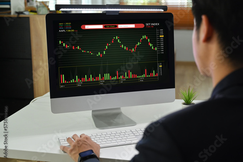 Rear view of man trader investor analyzing digital exchange stock market charts graphs on computer screen