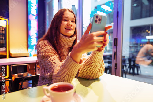 Portrait of young woman using mobile phone while sitting in comfortable coffee shop