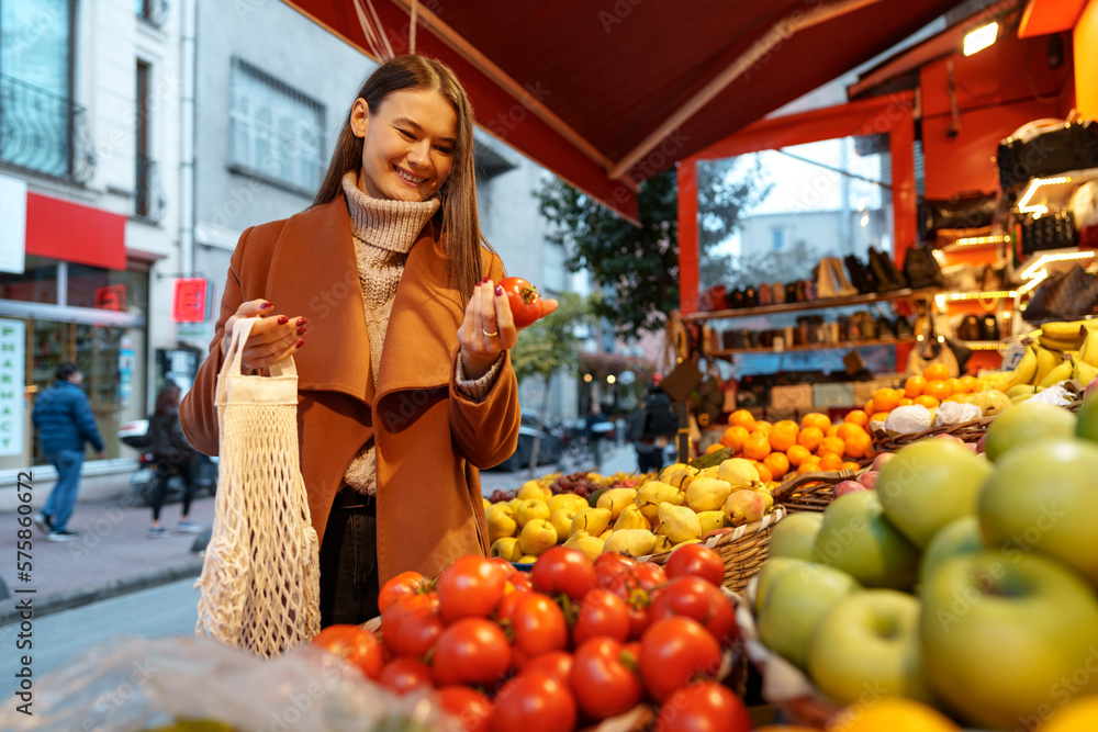 Good looking young woman standing in front of fruit shelves buying groceries in the street