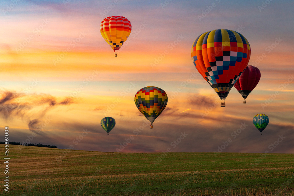 Fototapeta premium Colorful hot air balloons flying over field at sunset.