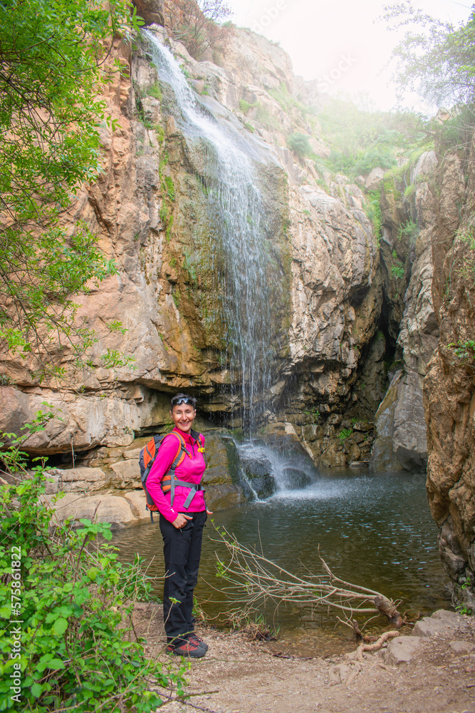 smiling woman posing in front of large waterfall in the rocks smiling woman posing in front of large waterfall in the rocks