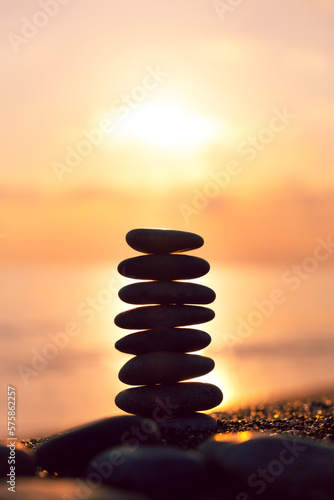Vertical İmage, Balanced pebble pyramid silhouette on the beach at sunset. Zen stones on the sea beach, meditation, spa, harmony, calmness, balance concept.