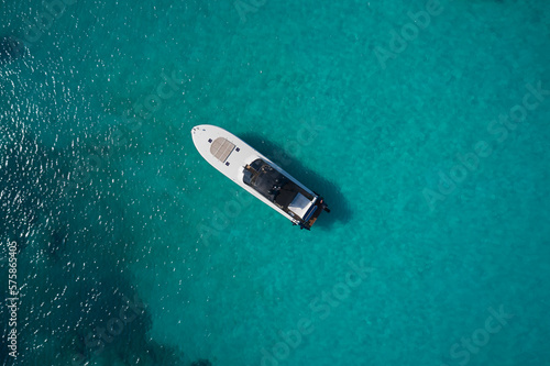 White modern boat with motor on blue transparent water aerial view. Big white motor boat anchored on the blue sea top view.