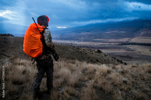 Deer hunter walking through Colorado backcountry at sunrise as thunderstorm approaches, Colorado, Colorado, USA photo