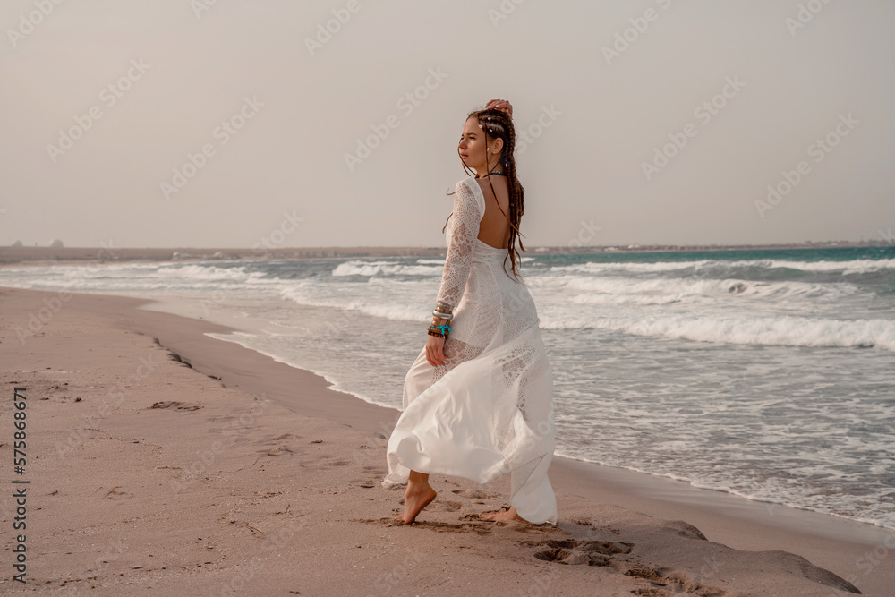 Model in boho style in a white long dress and silver jewelry on the beach. Her hair is braided, and there are many bracelets on her arms. Model in boho style in a white long dress and silver jewelry on the beach. Her hair is braided, and there are many bracelets on her arms.
