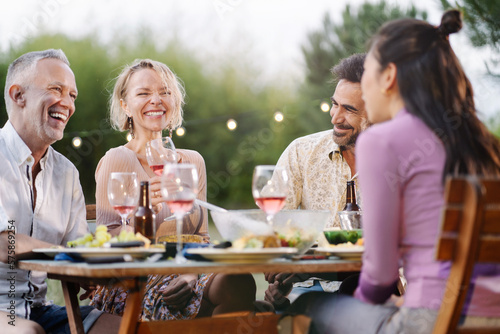 Photo Family friends having dinner around table in a garden in summer, drinking wine,