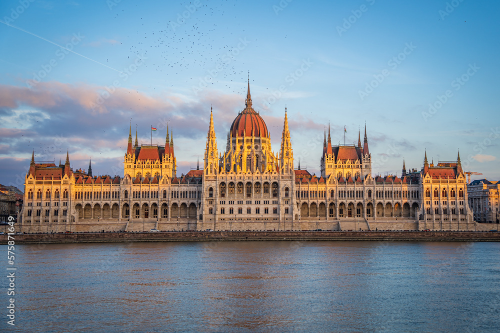 Fototapeta premium Budapest Parliament from across Danube river at Sunset, Hungary. Beautiful golden light on building rooftop. Evening sky with pink clouds.
