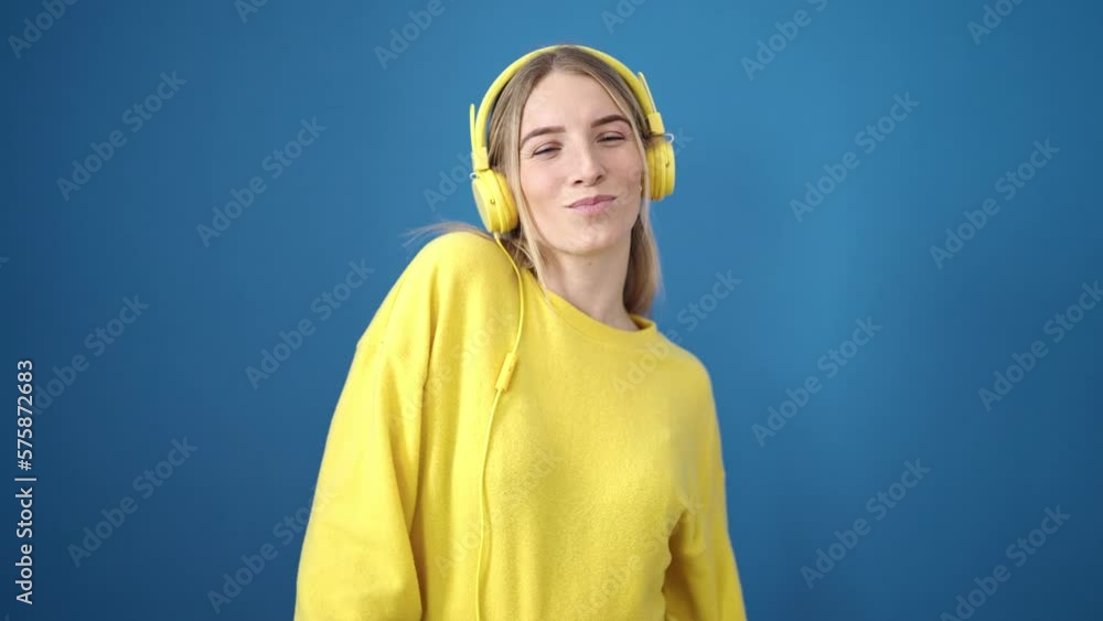 Young blonde woman dancing wearing headphones over isolated blue background Young blonde woman dancing wearing headphones over isolated blue background