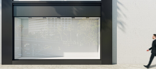 Man walking by sunlit wall background with place for your advertising poster near empty shop window with space for your product presentation in modern building area outdoors, mock up
