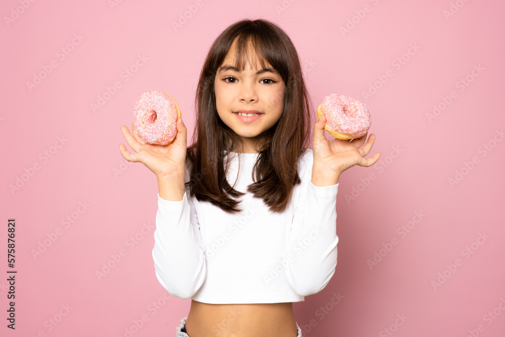 Pretty little girl having fun with some sweet food holding a couple of donuts and smiling isolated over pink background. Pretty little girl having fun with some sweet food holding a couple of donuts and smiling isolated over pink background.