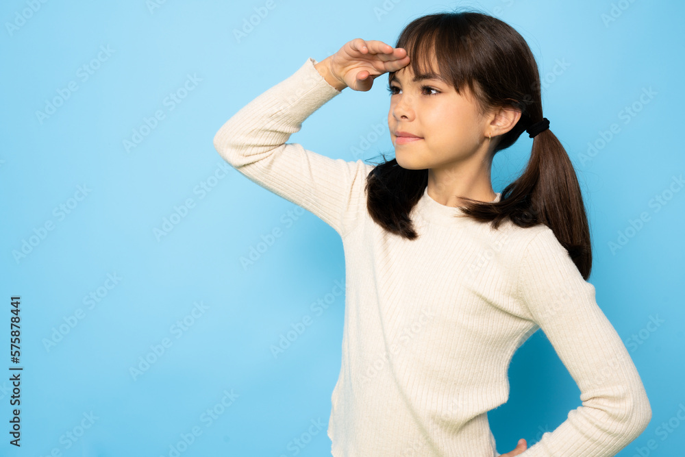 Young beautiful child girl wearing white t-shirt standing over isolated blue background very happy and smiling looking far away with hand over head. Searching concept. Young beautiful child girl wearing white t-shirt standing over isolated blue background very happy and smiling looking far away with hand over head. Searching concept.