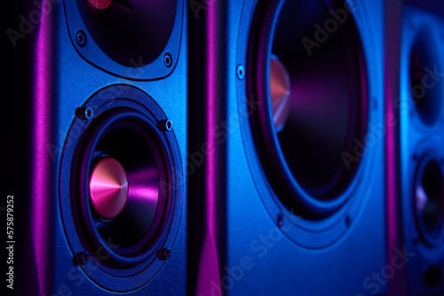 Two sound speakers and subwoofer on dark background with neon lights. Set for listening music. Audio equipment