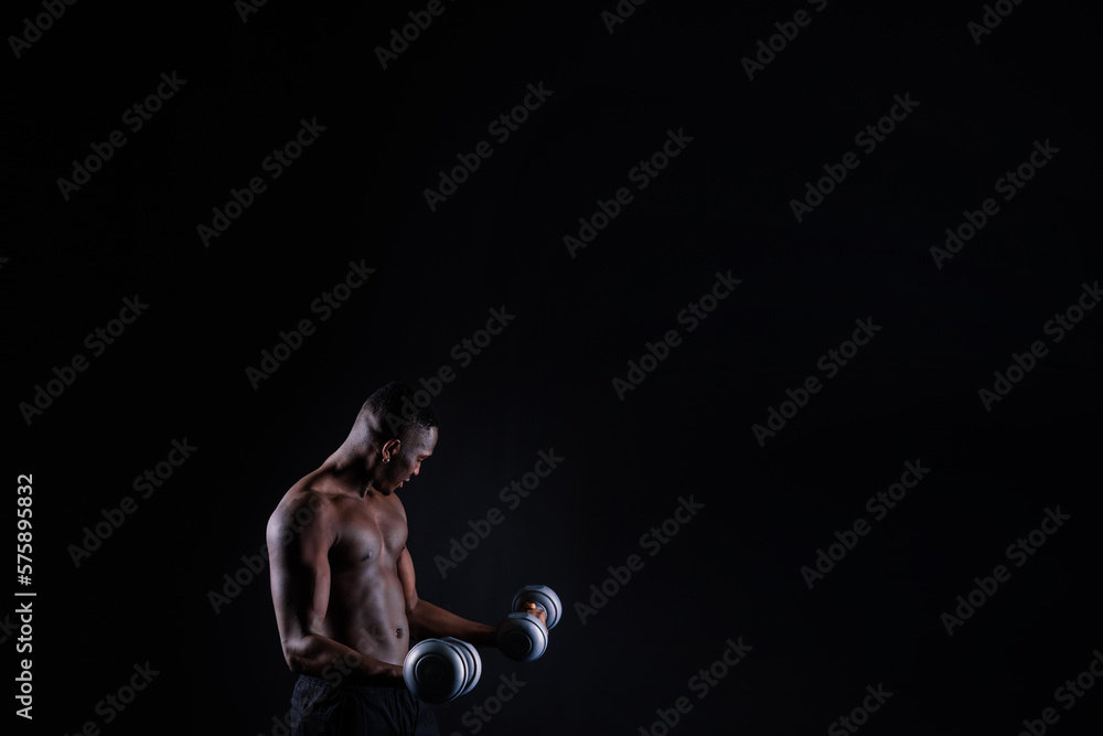 Isolated african muscular man with dumbbells on dark studio background. Strong shirtless black guy