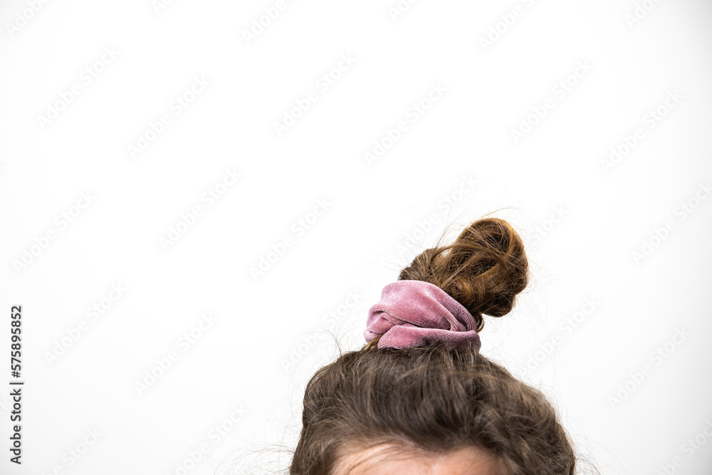 Messy hair bun female brunette closeup with grey white background and copy space, A disheveled bunch on the head of a dark-haired woman. The hair is tied with a pink elastic band. Modern fast Messy hair bun female brunette closeup with grey white background and copy space, A disheveled bunch on the head of a dark-haired woman. The hair is tied with a pink elastic band. Modern fast