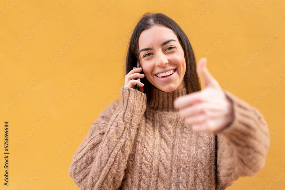 Young brunette woman at outdoors keeping a conversation with the mobile while doing thumbs up Young brunette woman at outdoors keeping a conversation with the mobile while doing thumbs up