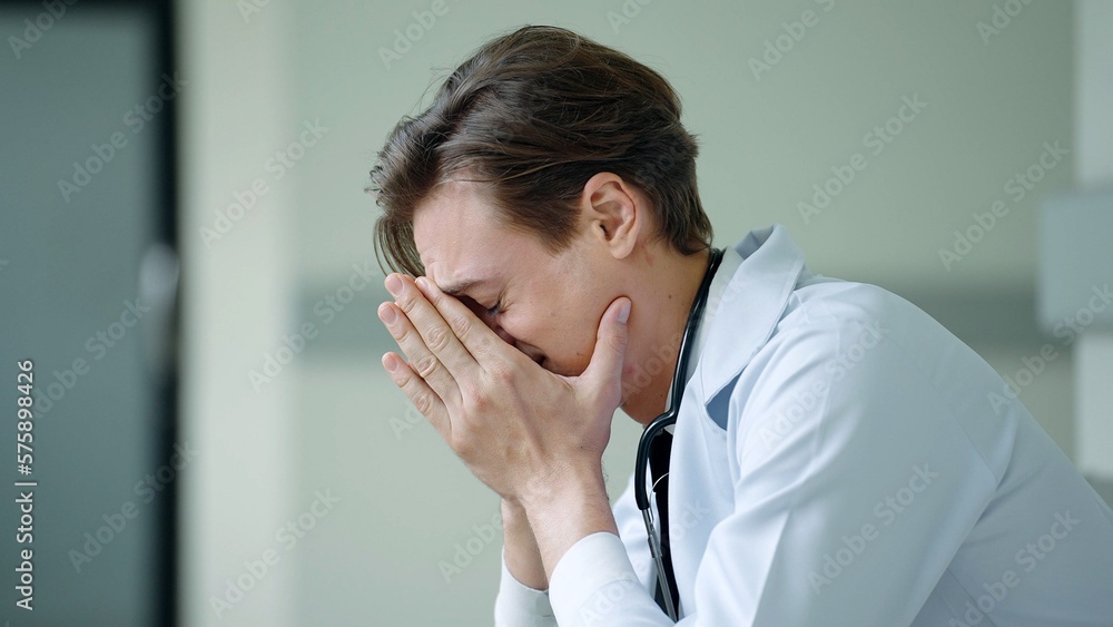 Emotionally depressed doctor sitting at hospital. Overworked male doctor in despair or tired Emotionally depressed doctor sitting at hospital. Overworked male doctor in despair or tired