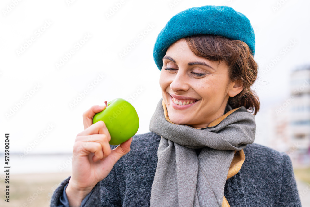 Brunette woman with an apple at outdoors with happy expression Brunette woman with an apple at outdoors with happy expression
