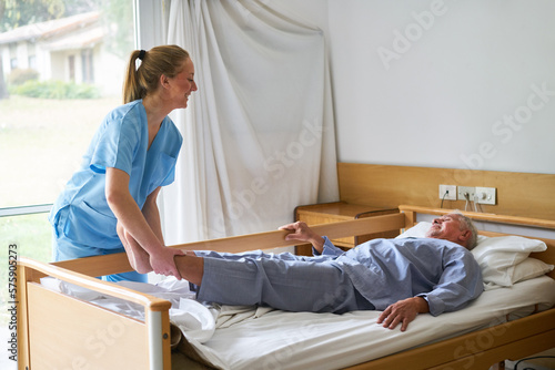 Fototapete Nurse lifting legs of elderly man lying in bed