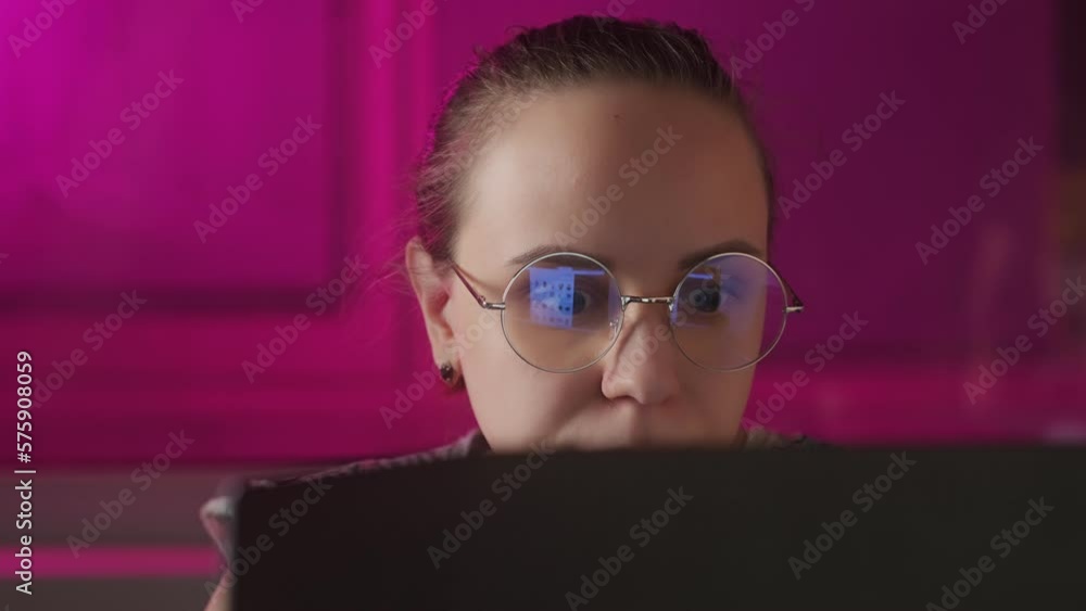Young thoughtful woman in glasses sitting at laptop computer in dark room. Pensive female working on laptop. Freelance concept. Young thoughtful woman in glasses sitting at laptop computer in dark room. Pensive female working on laptop. Freelance concept.