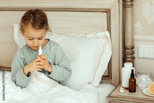 Sick child on bed in pajamas at home child treats runny nose with nasal spray. release your stuffy nose. children with nasal drops take medicine