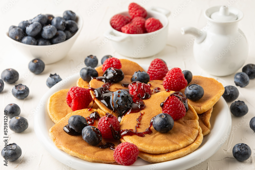 Top view of pancakes with caramel on plate with blueberries and raspberries with bowls and jar on white table, selective focus, horizontal Top view of pancakes with caramel on plate with blueberries and raspberries with bowls and jar on white table, selective focus, horizontal
