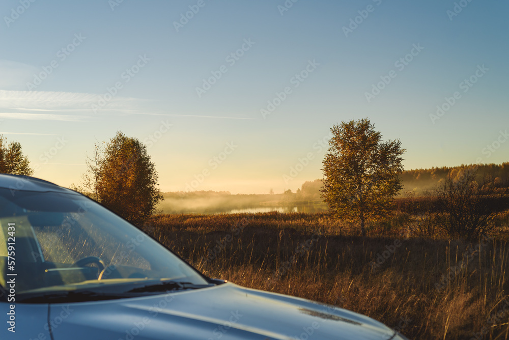 Fototapeta premium Traveling by car concept with vehicle in foreground and beautiful foggy evening landscape in background