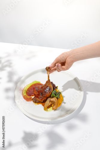 Female hand holding duck leg in restaurant. Woman eat duck confit. Eating process. Trendy food menu Hand holding duck leg on summer dining