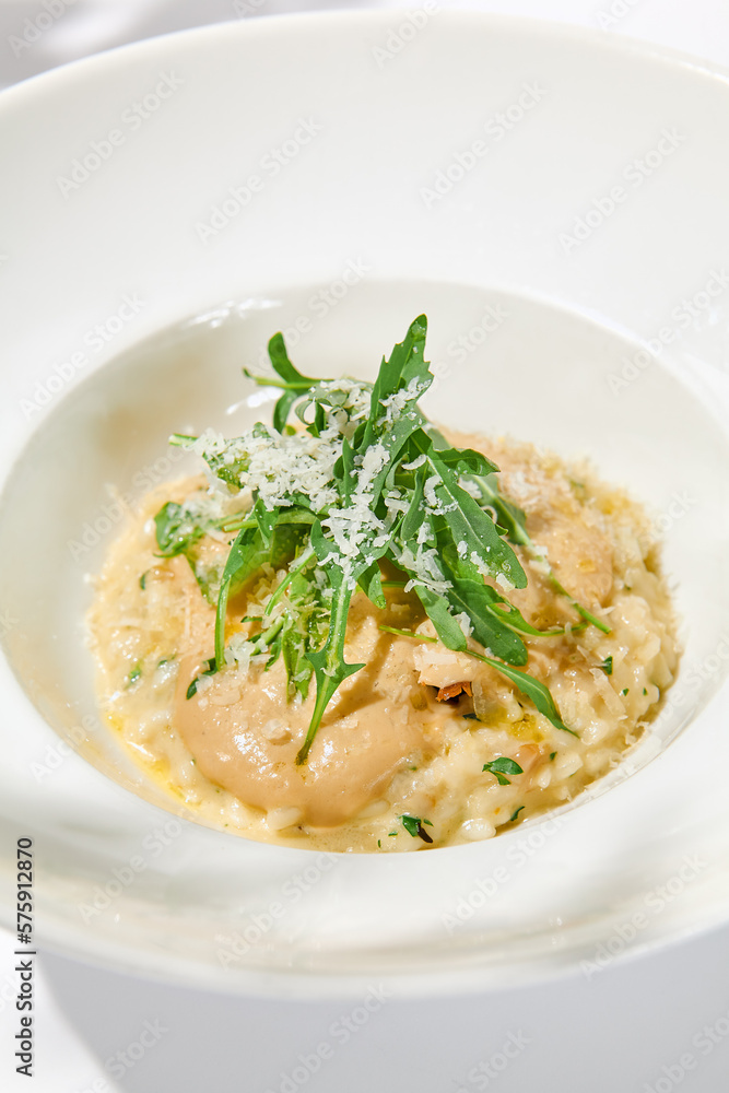 Italian cheese risotto on white plate. Creamy risotto topped parmesan cheese and espuma. Italian risotto with cheese on light background with shadows of leaves Simple italian menu Italian cheese risotto on white plate. Creamy risotto topped parmesan cheese and espuma. Italian risotto with cheese on light background with shadows of leaves Simple italian menu