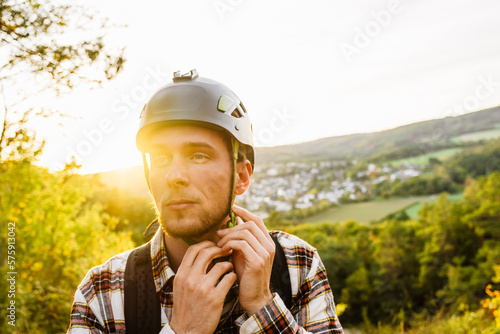Valokuva Young man putting on helmet while standing on hillside