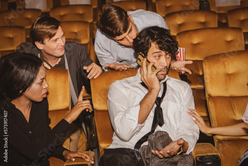 Concept Etiquette in the cinema Do not talk on the phone to disturb others : Selfish men talking on the phone among moviegoers annoy those around them who resent their bad behavior. photo