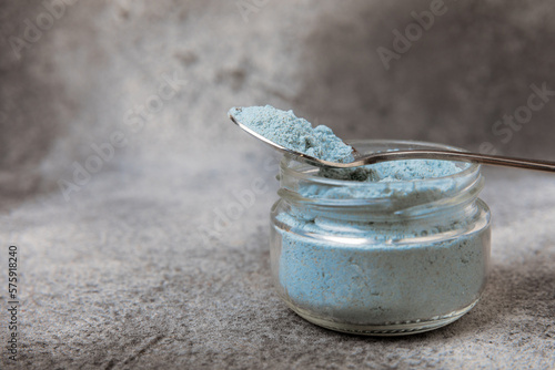 Blue spirulina powder in a bowl on a black textured surface. Natural vegan superfood. Healthy food supplement. Phycocyanin extract. Place for text. Place for a copy. photo