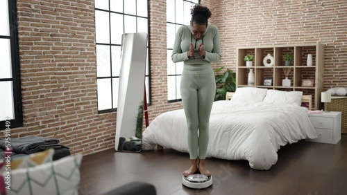 African american woman smiling confident measuring weight using weighing machine at bedroom