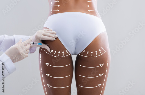 Young slim black woman in white bikini with abstract lines gets injection from beautician in hips