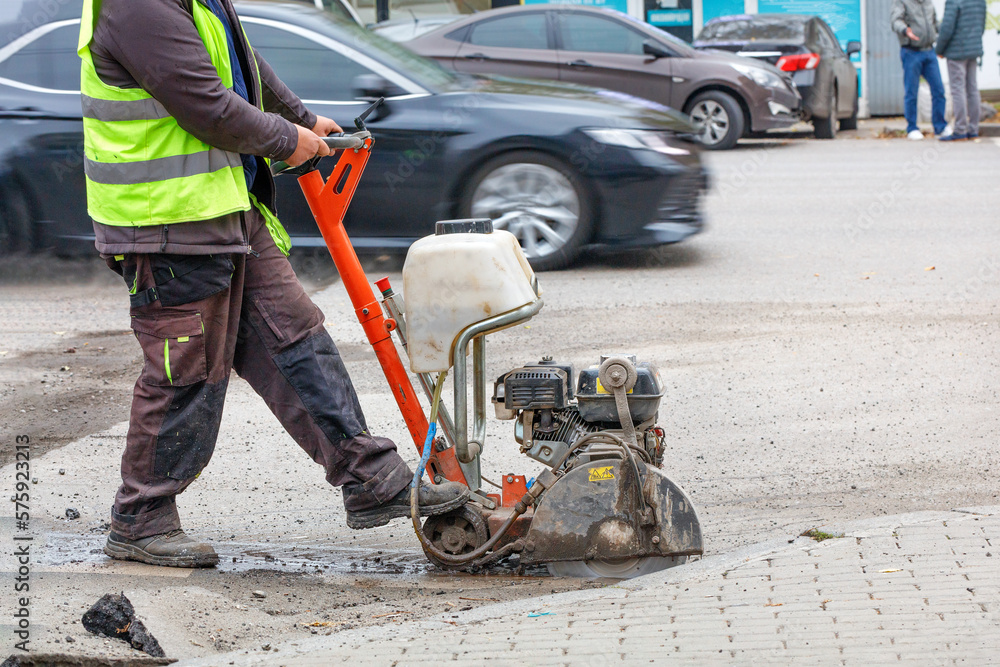 A road worker cuts with a petrol cutter and a diamond wheel the old asphalt on the carriageway of a city street.