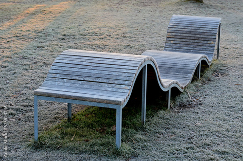 design bench in the shape of a wavy line. wooden paneling on a metal galvanized frame. The bench is atypical to order in a city park for young people and unusual sitting and lying, icing, winter, cold