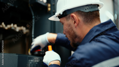 Close-up of Caucasian production engineer in safety wear inspecting CNC machine to fix an error. A male factory worker is maintaining industrial machine that is used to control the production line.