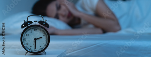 Obraz na plátne Close-up alarm clock on the table have a sleepless woman as background