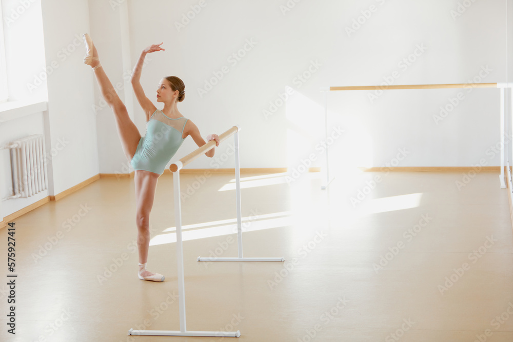 Beautiful flexible teen girl, ballet dancer training at dance school with ballet barre on daytime with sunlight. Concept of classical ballet, dance art, education, beauty, choreography Beautiful flexible teen girl, ballet dancer training at dance school with ballet barre on daytime with sunlight. Concept of classical ballet, dance art, education, beauty, choreography