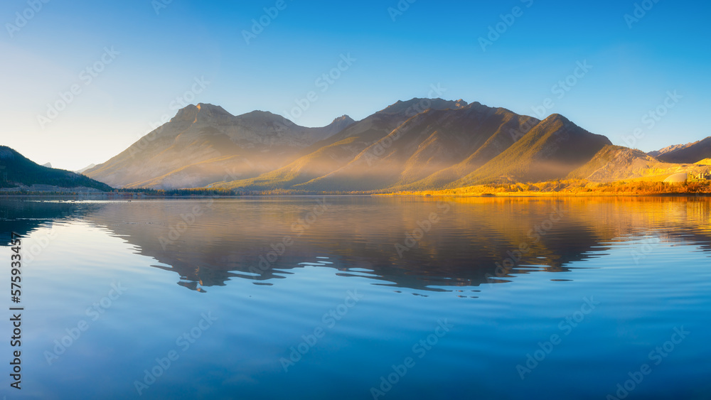 Obraz premium Lake and mountains in a valley at dawn. Reflections on the surface of the lake. Mountain landscape at sunrise. Foggy morning. Natural landscape with bright sunshine.