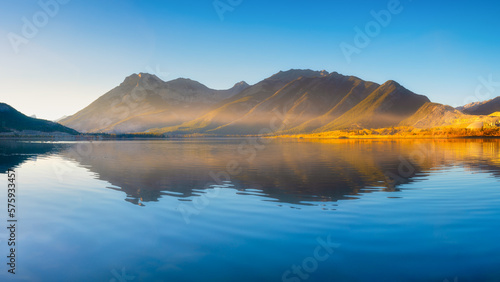 Lake and mountains in a valley at dawn. Reflections on the surface of the lake. Mountain landscape at sunrise. Foggy morning. Natural landscape with bright sunshine.