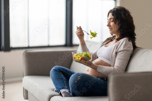 Pregnancy Nutrition. Young pregnant woman eating vegetable salad while relaxing at home