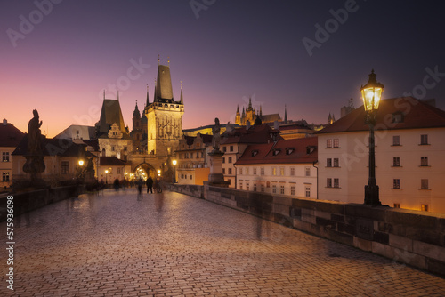 Charles bridge with silhouettes of tourists at night. Bridge towers and Prague Castle in gothic style, largest ancient castle in the world