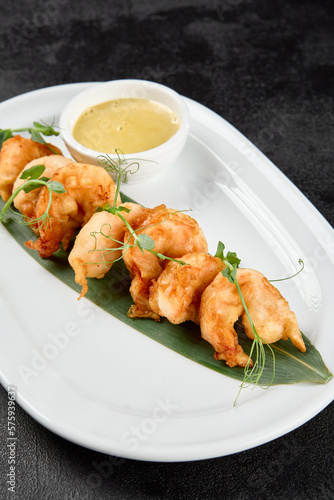 Appetizer of deep-fried shrimps with sauce. Crispy shrimps in tempura on black background. Fried prawns in asian style on dark concrete table. Asian prawns with sauce in minimal style.