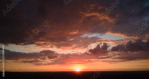 Bright colorful sunset sky with setting sun and vibrant clouds over dark landscape