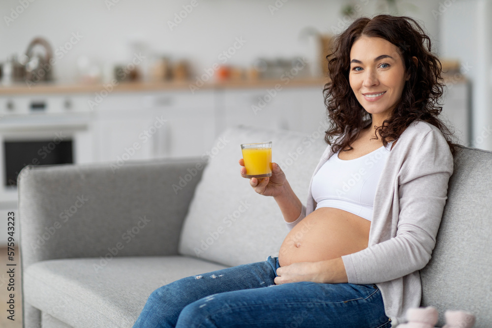 Young Pregnant Woman Holding Glass With Orange Juice While Relaxing On Couch