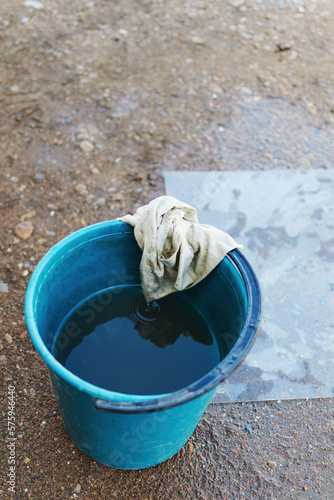 Angle top view outdoors on the ground there is a blue bucket with dirty water and an old wet shabby rag on it, copy space.
