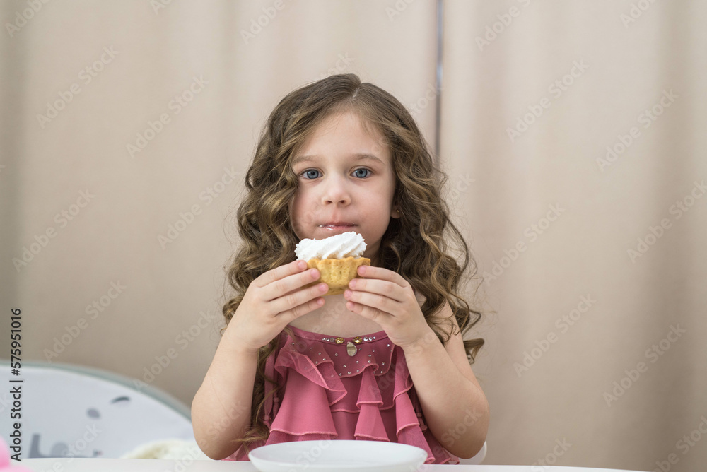 A little girl is eating a birthday cake at white table in light room.